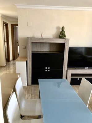 Una sala moderna con una larga mesa de comedor, sillas blancas, un televisor de pantalla plana y una estatua decorativa de Buda.