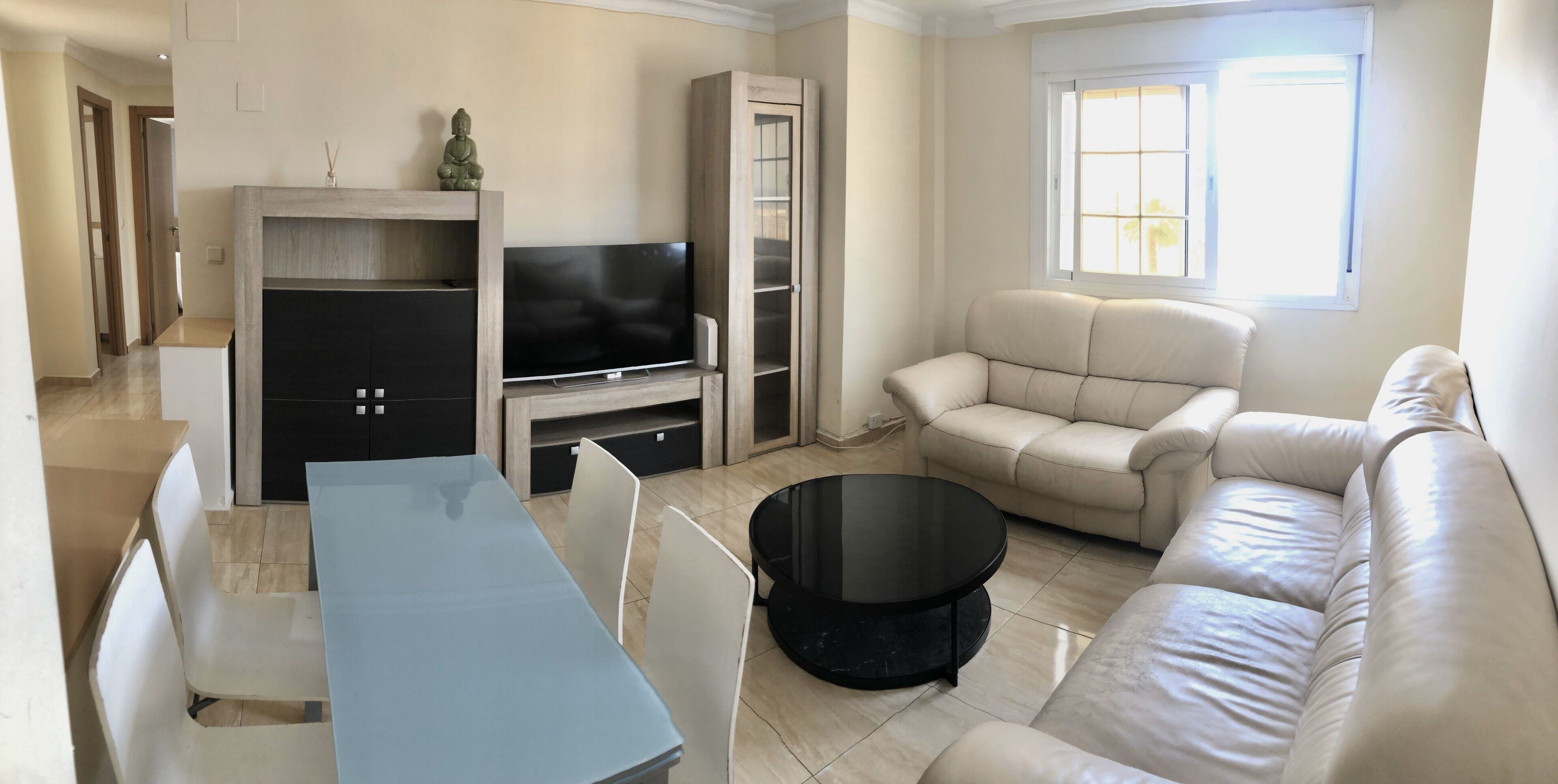Una sala de estar con un sofá, un televisor, una mesa de centro y una mesa de comedor.
