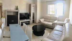 Una sala de estar con un sofá, un televisor, una mesa de centro y una mesa de comedor.
