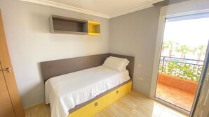 Un dormitorio con una cama, una pequeña estantería y vistas a un balcón con plantas.