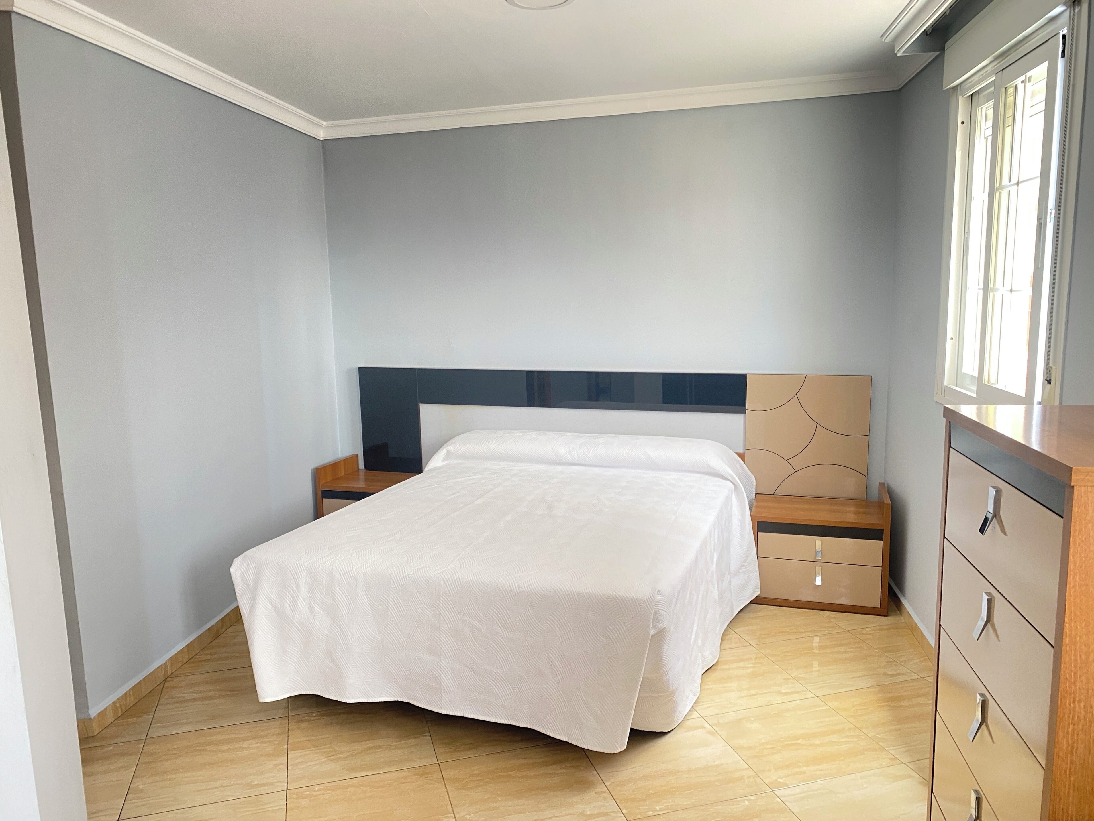 Un dormitorio con cama, mesitas de noche, cómoda y ventana.