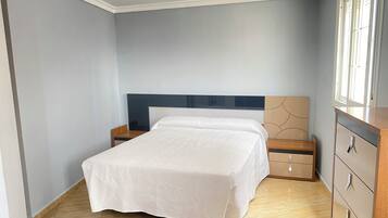 Un dormitorio con cama, mesitas de noche, cómoda y ventana.