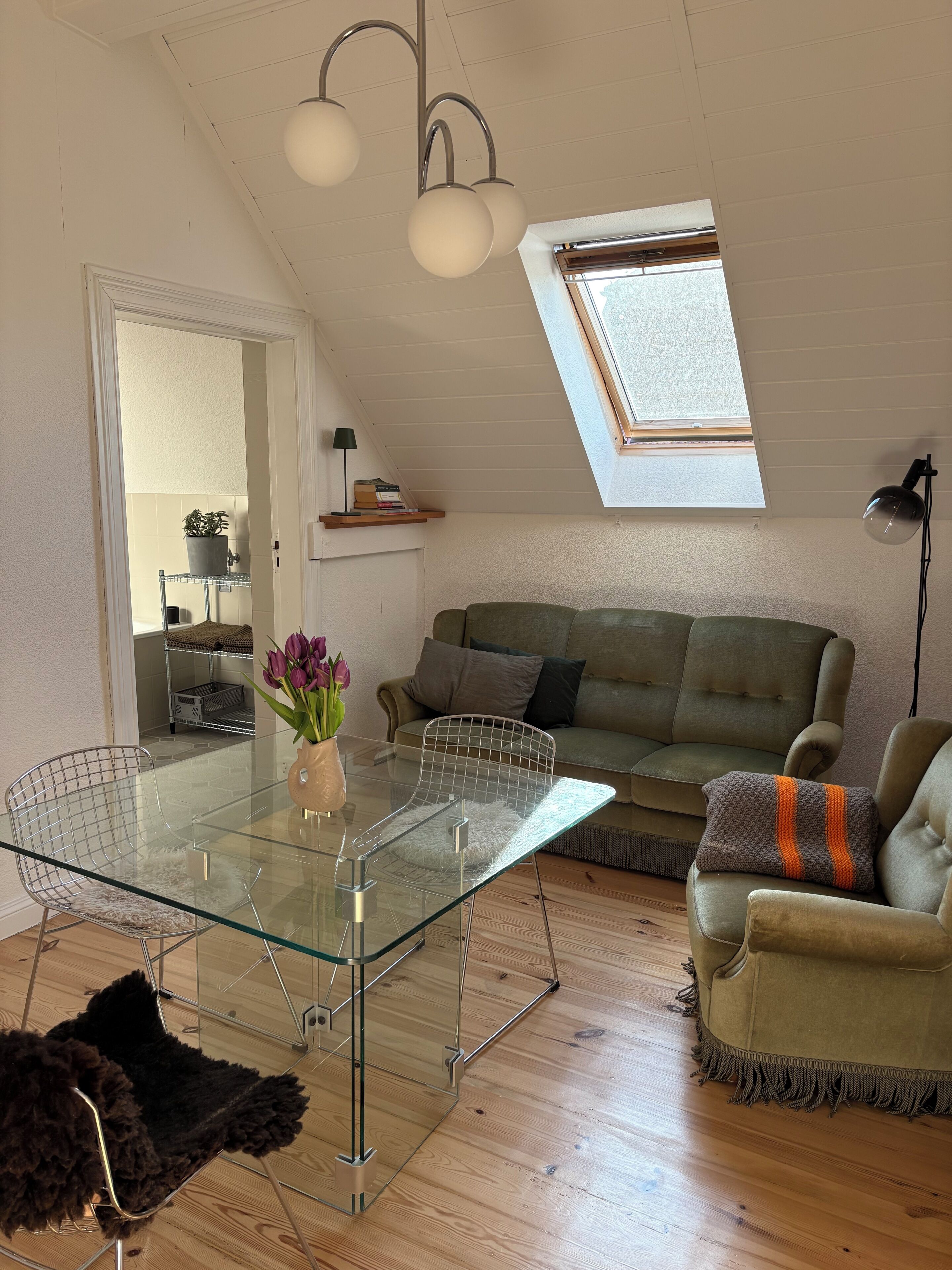 A loft-style living space with a glass dining table, a sofa, and a skylight.