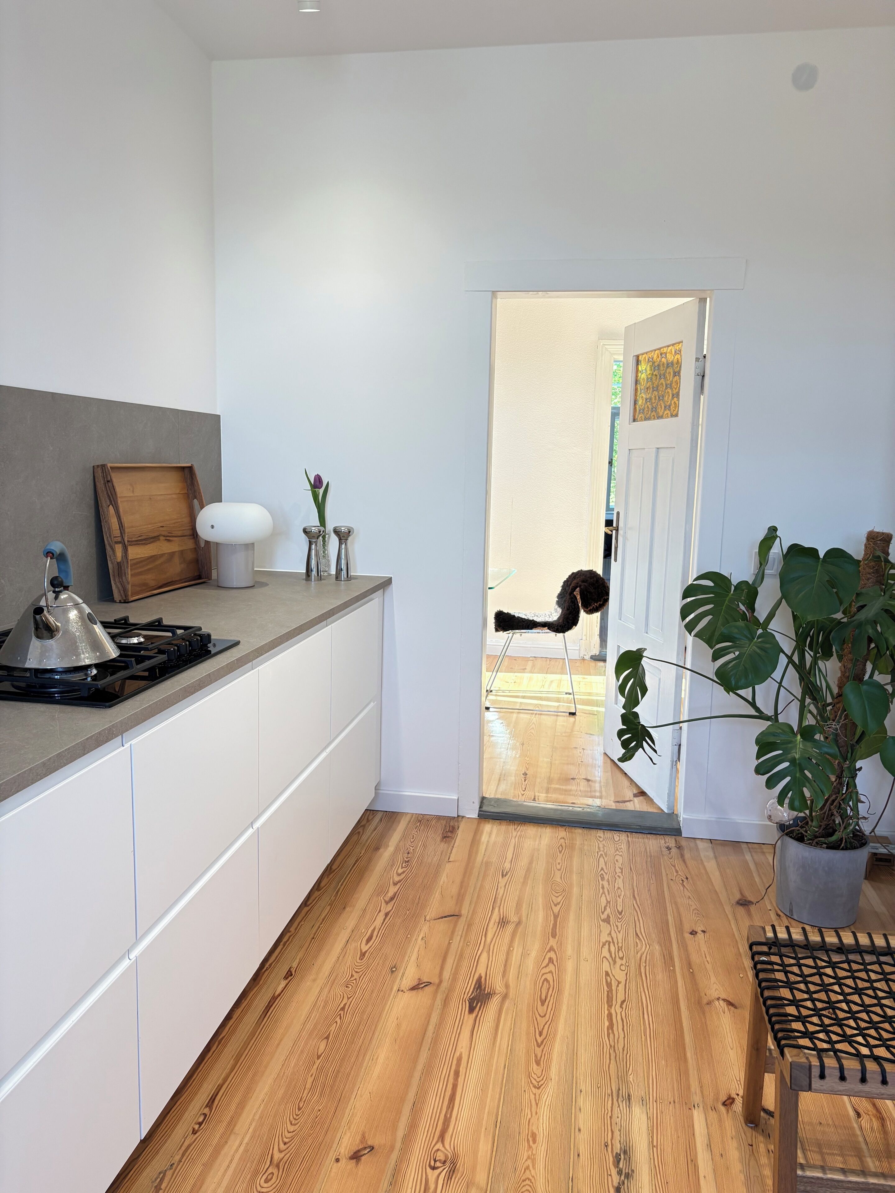 A modern kitchen with white cabinets, a wooden floor, and a view into a dining area.