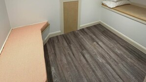 Ein Zimmer mit einem Bett, einer Bank, einem Kleiderständer und einem Regal mit Kissen.
