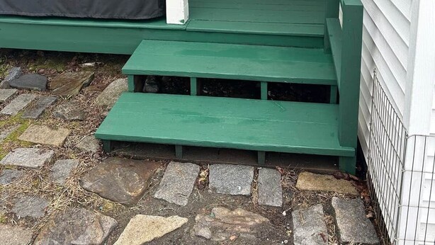 Eine Veranda mit überdachter Grillgelegenheit, einer weißen Tür mit Fenster und einer grünen Bank.