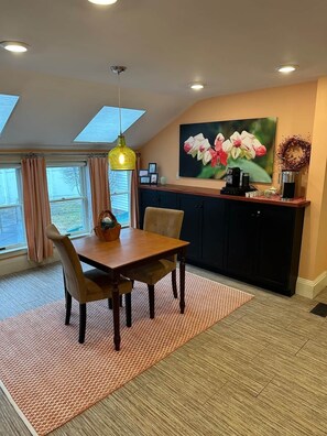 A dining area with a table, chairs, a pendant light, a painting, and a kitchen area with cabinets. - Beautiful historic home w/view of Kennebec River (Bath)