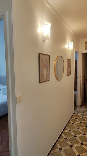Ein Korridor mit Schachbrettboden, einem Bett im Hintergrund und Wandleuchten.