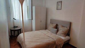 Un dormitori amb llit, armari, taula petita i làmpada.