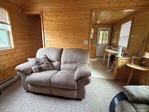 A cozy cabin interior with a sofa, a dining table, and a window. - Secluded, rustic 1-bedroom cabin w/ loft located on working ranch in Rapid City (Rapid City)