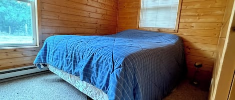 Um quarto com cama, paredes de madeira, uma janela e uma porta.