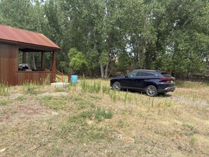 A cabin with a metal roof, a parked car, and a forested area. - Secluded, rustic 1-bedroom cabin w/ loft located on working ranch in Rapid City (Rapid City)