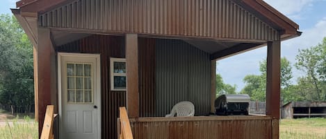 Une cabane rustique avec une véranda en bois, une porte et une petite dépendance attenante.
