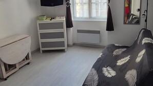 Un dormitorio con una cama, televisión, cómoda, ventana con cortinas y espejo.