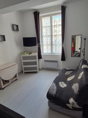 Ein Schlafzimmer mit einem Bett, einem Fernseher, einer Kommode, einem Fenster mit Vorhängen und einem Spiegel.