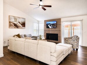 Ein Wohnzimmer mit Ecksofa, Flachbildfernseher an einer Holzwand montiert, Kamin und Deckenventilator.