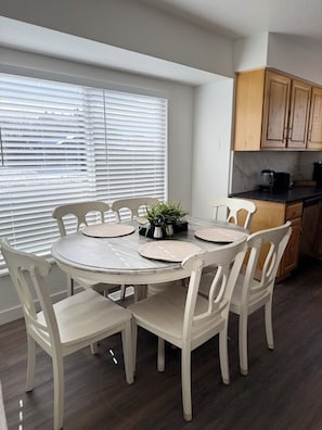 A dining area with a round table, white chairs, and a window with blinds. - Modern Home/ Near DIA & Anschutz Medical Campus (Denver)