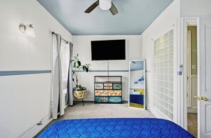 A bedroom with a bed, a ceiling fan, a flat-screen TV, a decorative cabinet, and a door leading to another room. - Spacious Historical Oasis (Allentown)