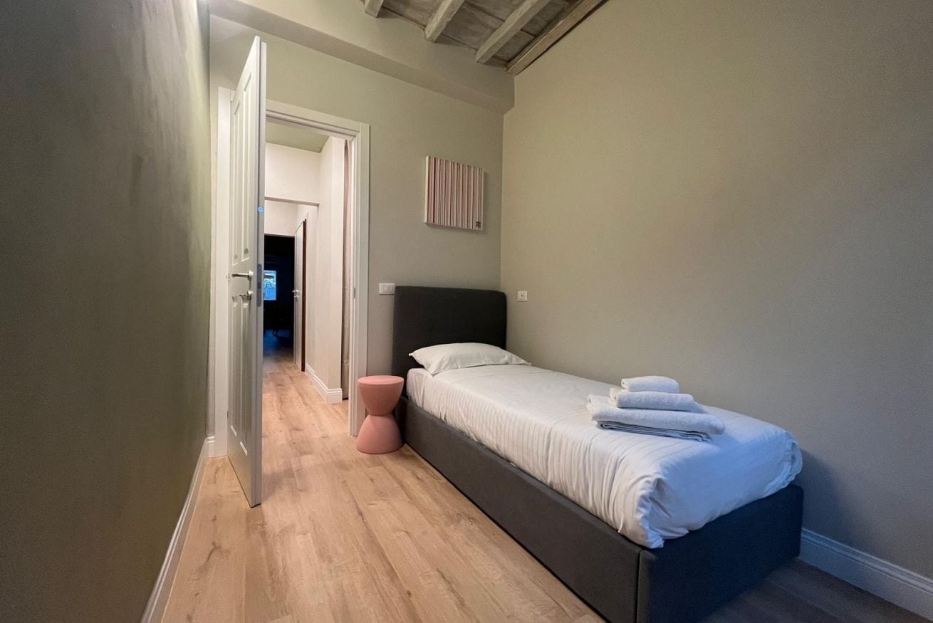 A bedroom with a single bed, a bedside table, and a door leading to another room.