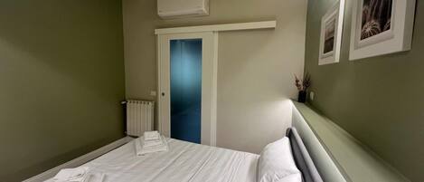 Habitación de hotel con cama, radiador, puerta y aire acondicionado instalado en la pared.