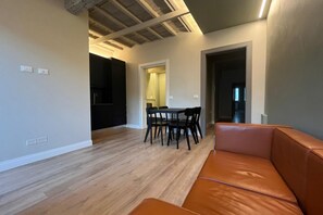 Ein modernes Wohnzimmer mit Ledersofa, einem Esstisch mit Stühlen und einer Küche im Hintergrund.