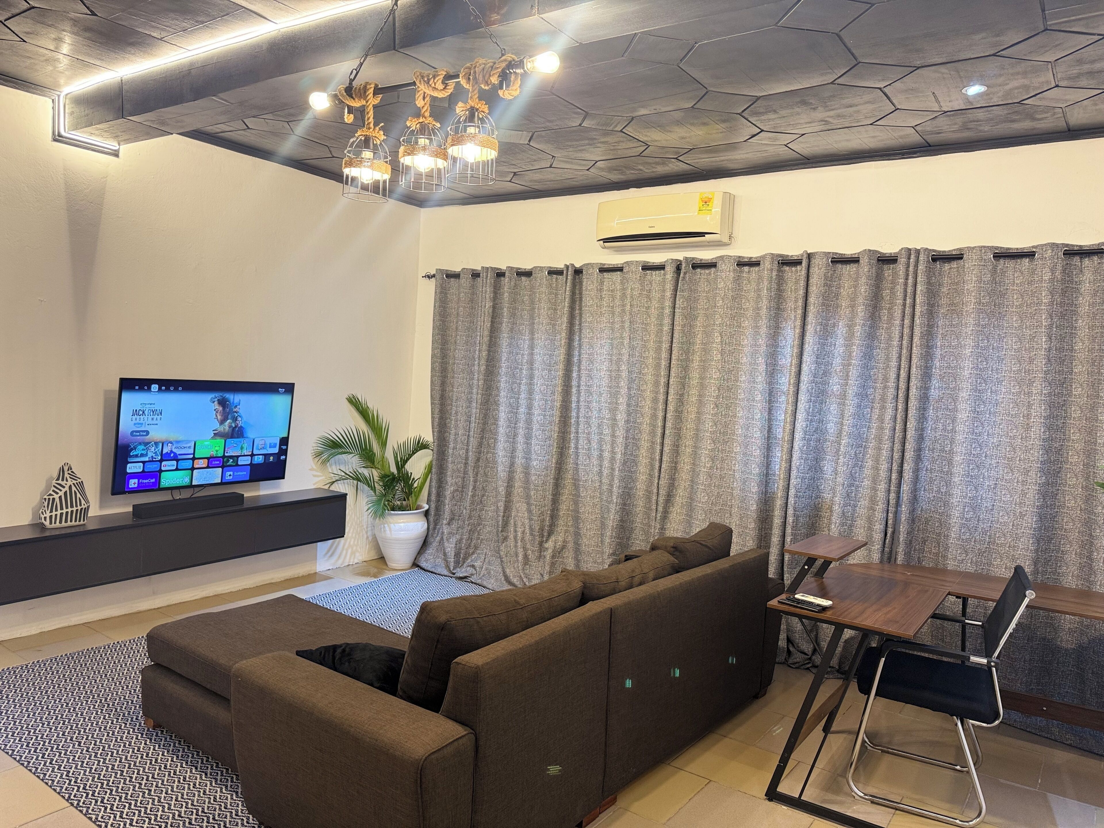 Un salon moderne avec un canapé d’angle, une table à manger avec des chaises, un téléviseur à écran plat fixé au mur et une plante en pot.