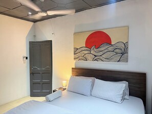 A bedroom with a bed, a door, a wall-mounted artwork, and a nightstand with a lamp. - City Centre Oasis (Accra)