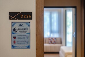 A hotel room with a wooden door, a sign with the number C226, and a multilingual notice on the wall. - Bellevue Beachfront Apartments (Choeng Thale)