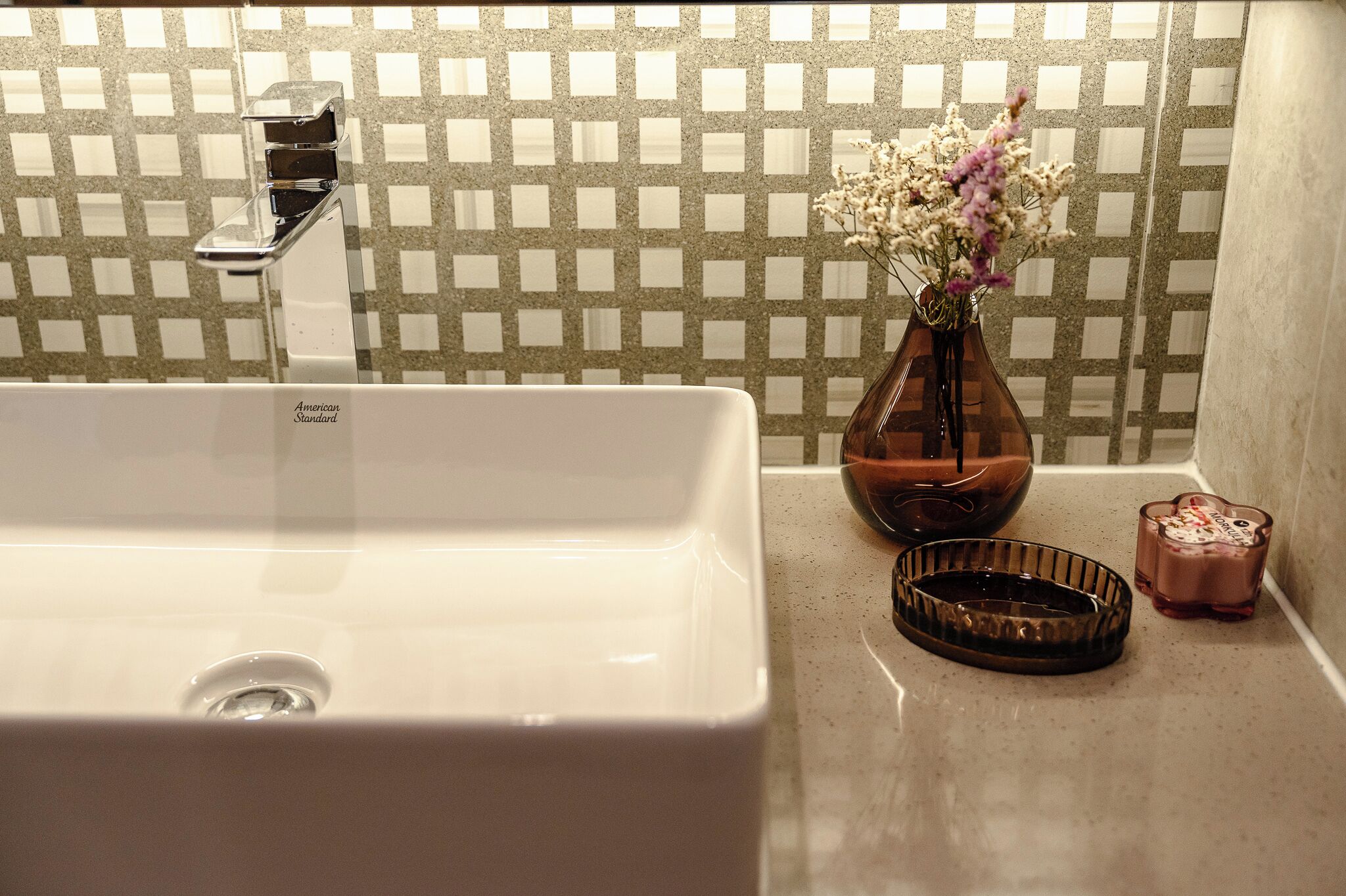 A bathroom with a white sink, a faucet, a vase with flowers, and a soap dish.