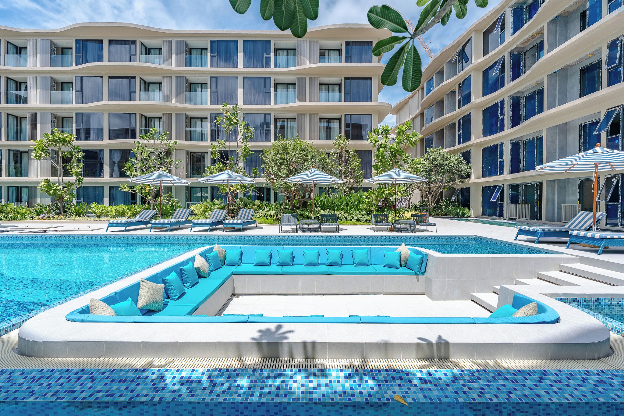 Un hotel con piscina, sillas de descanso y sombrillas.