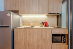A compact kitchen with a built-in microwave, a coffee maker, and a stainless steel refrigerator. - Bellevue Beachfront Apartments (Choeng Thale)