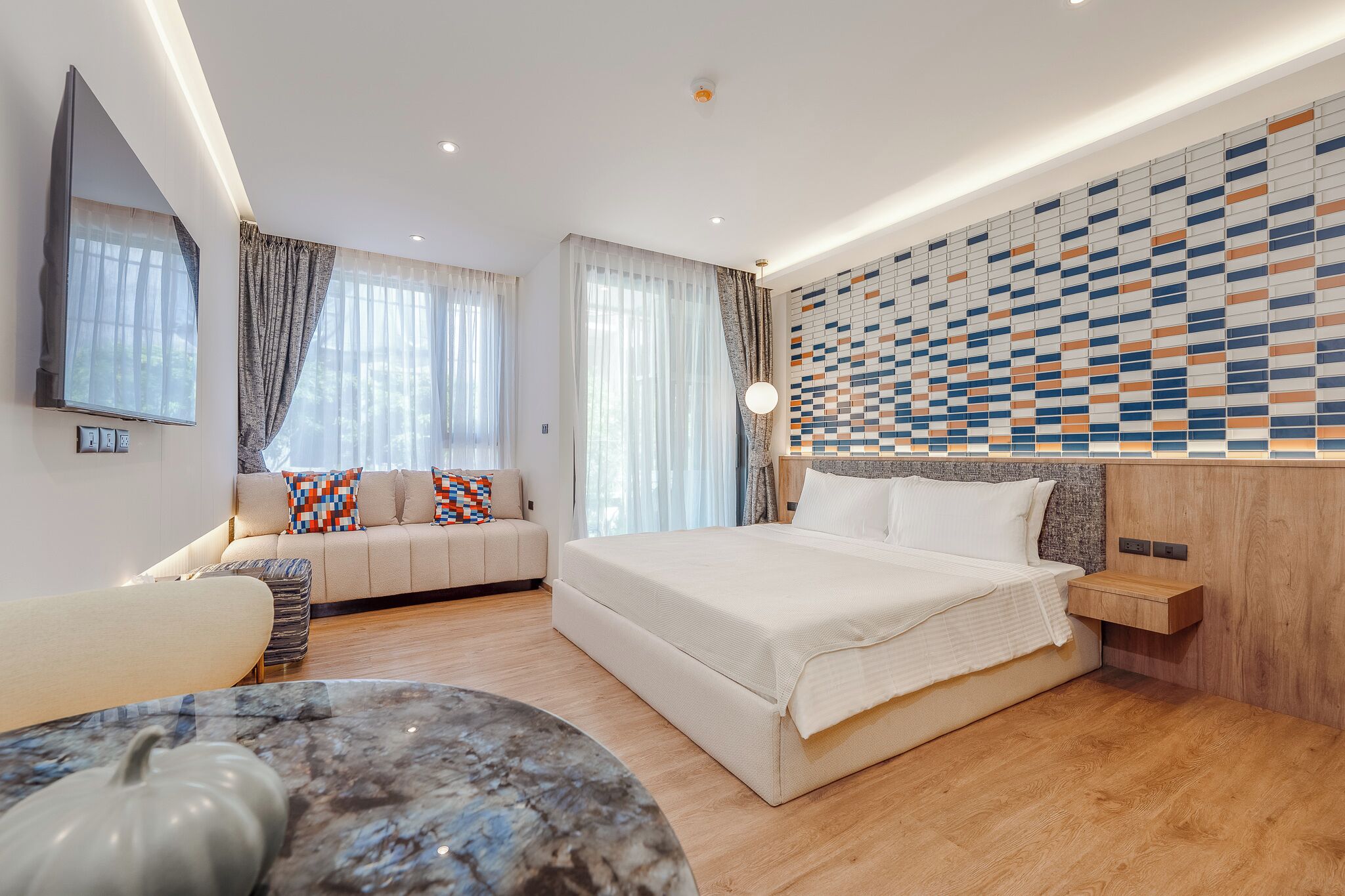 A modern bedroom with a large bed, a sofa, a marble coffee table, and a patterned wall.