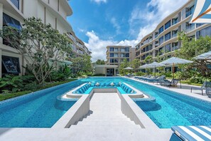 A modern hotel with a central swimming pool, lounge chairs, and a landscaped garden. - Bellevue Beachfront Apartments (Choeng Thale)