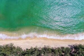 A beach with clear turquoise water, a sandy shore, and dense vegetation at the water's edge. - Bellevue Beachfront Apartments (Choeng Thale)