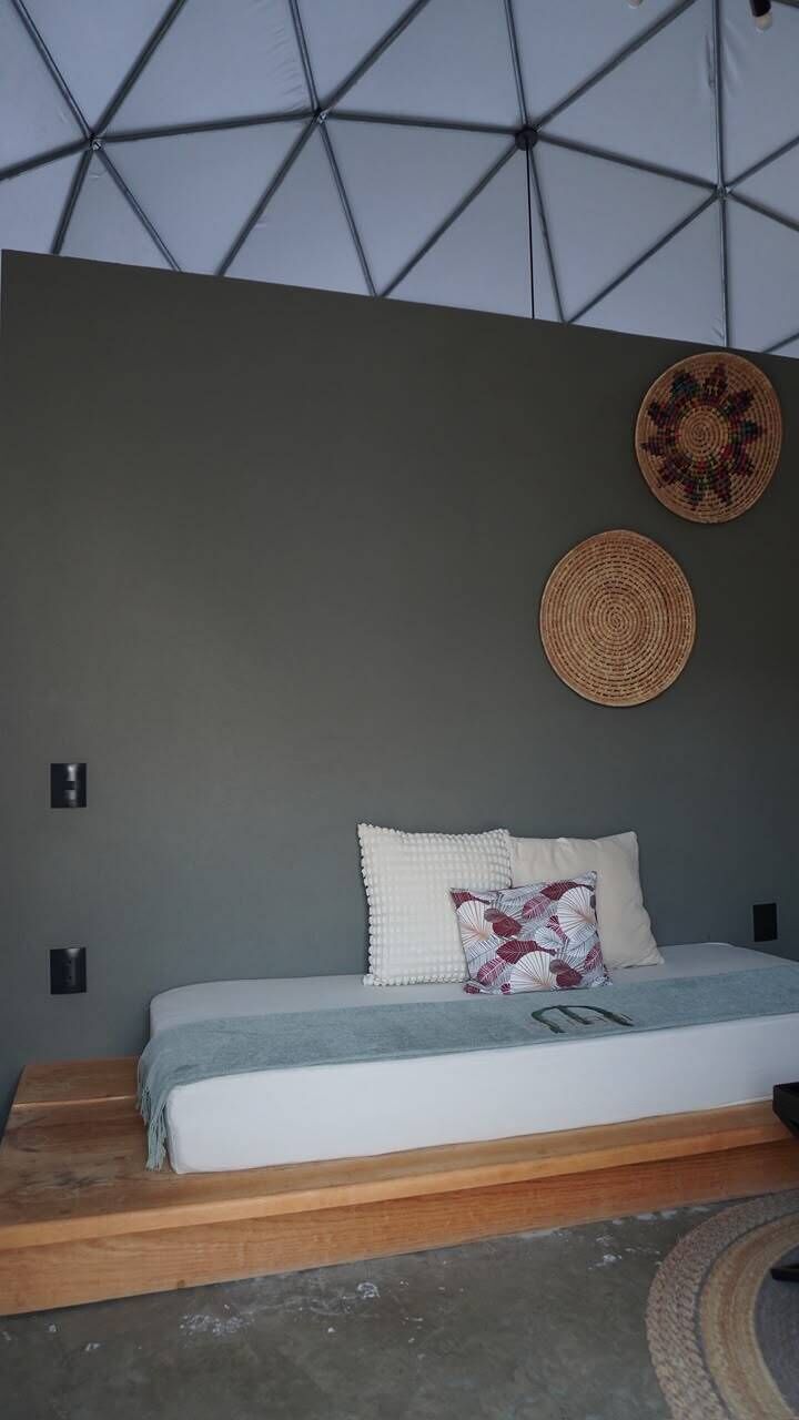 Un dormitorio con una cama, un adorno circular tejido en la pared y una estructura de techo geométrica.