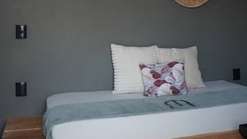 Un dormitorio con una cama, un adorno circular tejido en la pared y una estructura de techo geométrica.