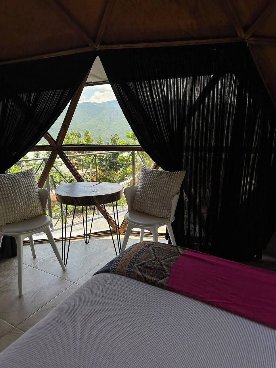 A room with a bed, two chairs, a small table, and a view of the outdoors.
