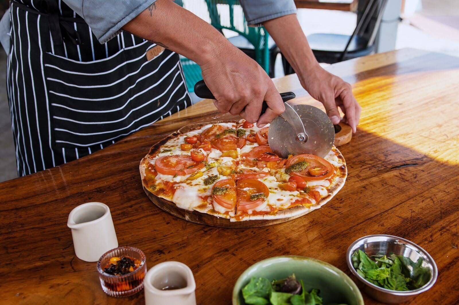 Una persona cortando una pizza sobre una mesa de madera.
