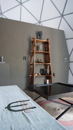 A room with a bed, a wooden ladder shelf, and a glass coffee table.