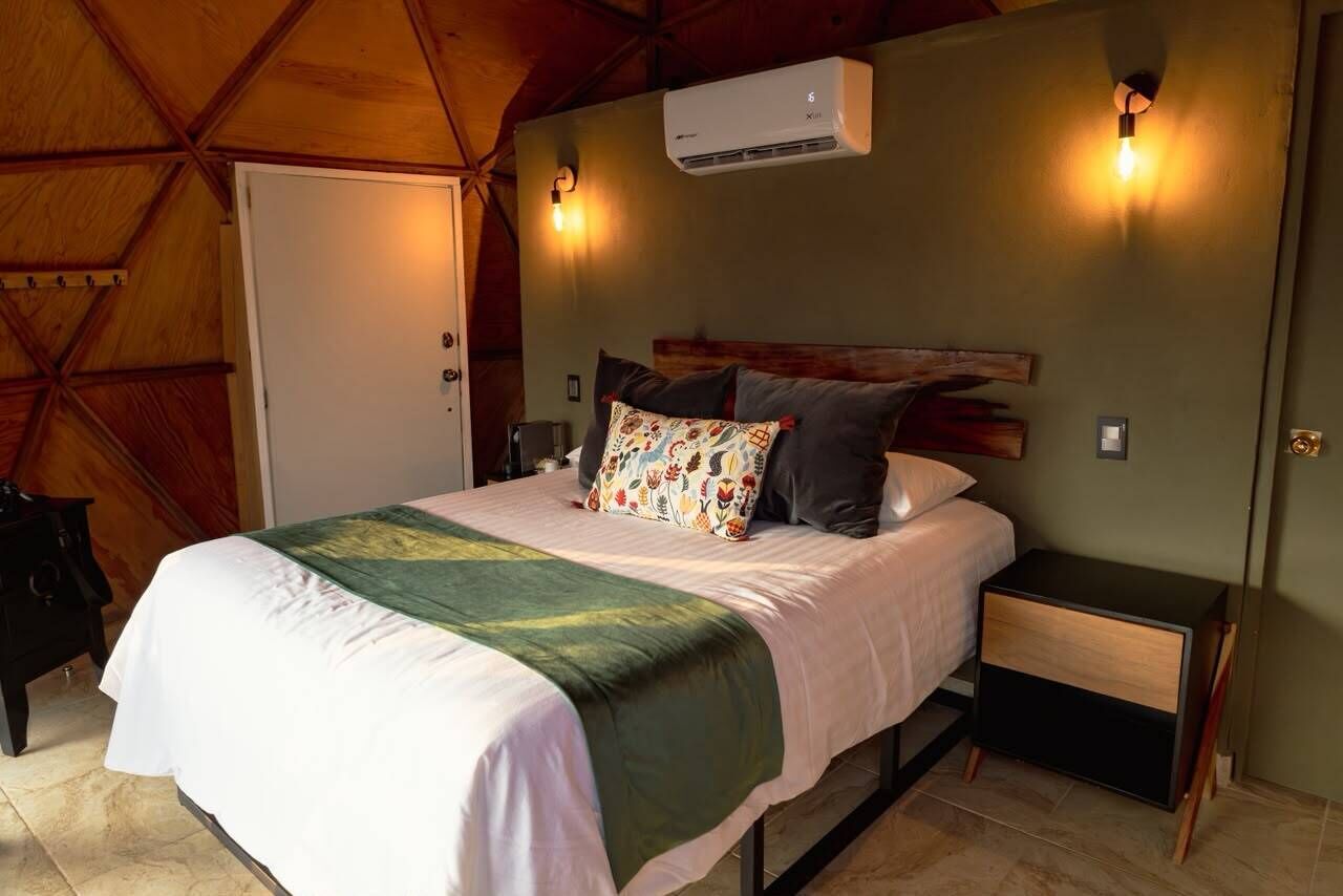 A bedroom with a bed, bedside tables, an air conditioning unit, and wall-mounted lighting.
