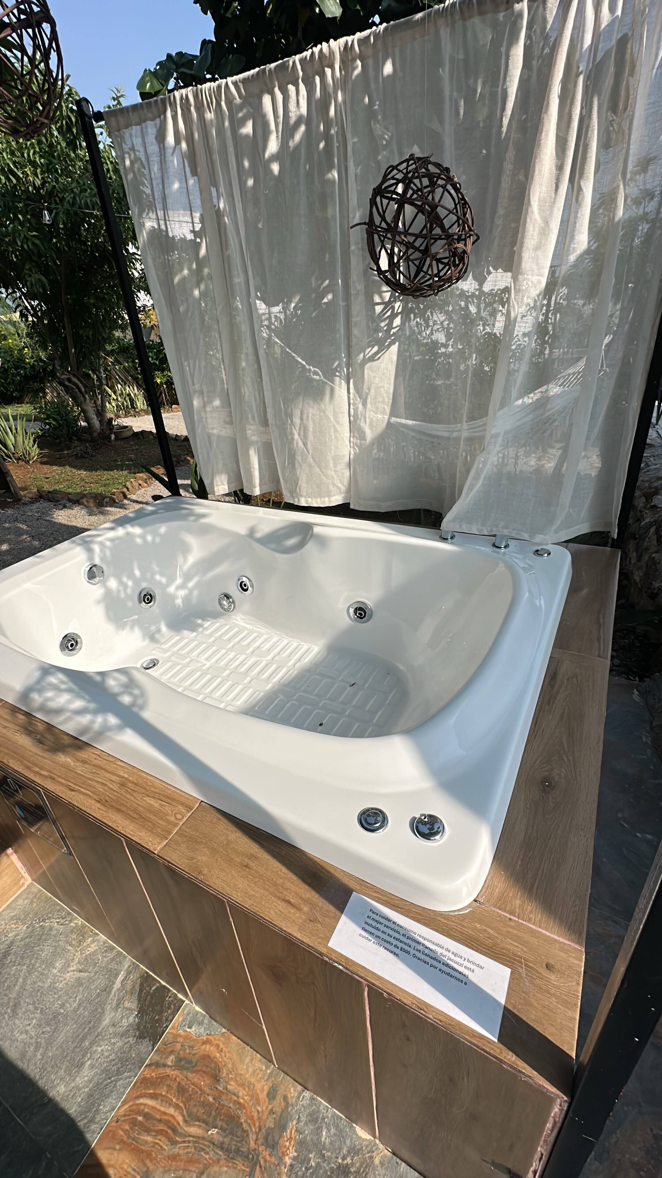 A white hot tub with four jets, surrounded by a wooden deck and a white curtain.