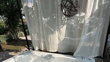 A white hot tub with four jets, surrounded by a wooden deck and a white curtain.