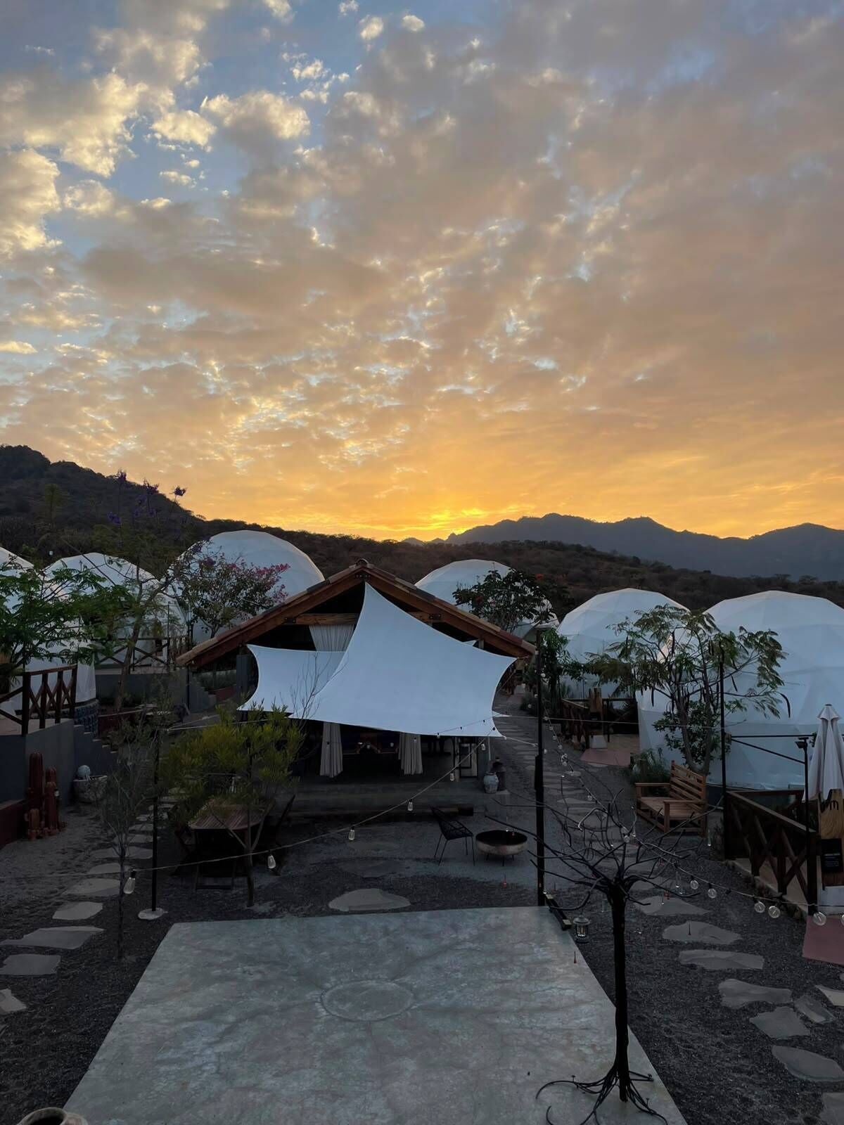 A resort with dome-shaped tents, a wooden structure, and a paved area with steps leading to a seating area.