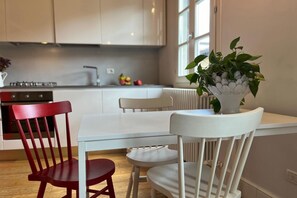 Een eetruimte met een witte tafel en stoelen, een rode stoel en een potplant.