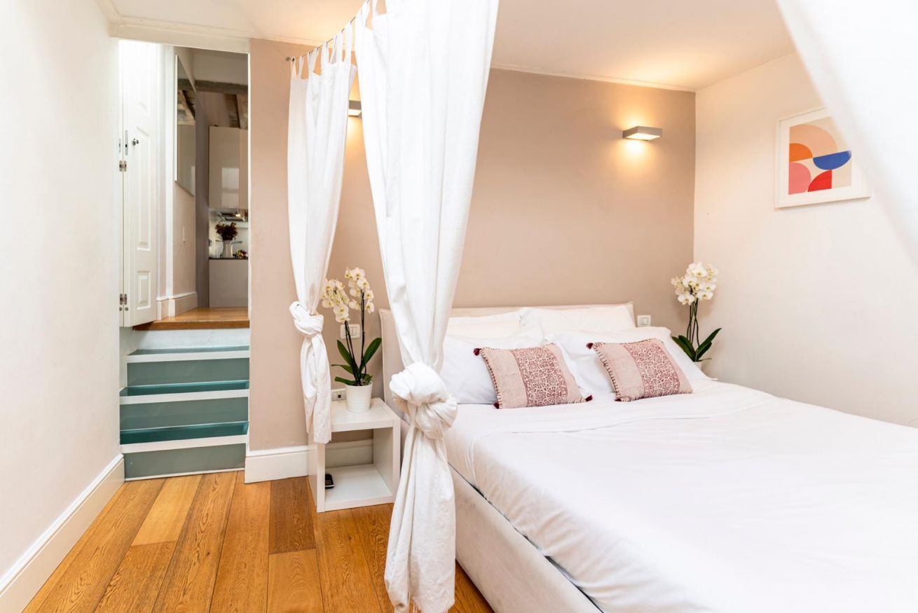 A bedroom with a bed, a staircase, and a wall-mounted light fixture.