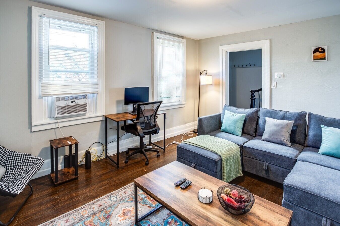 A living room with a sofa, a desk with a computer, a lamp, and a patterned rug.