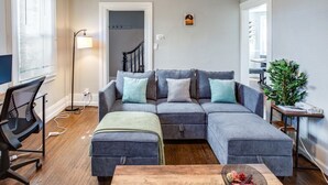 A modern living room with a grey sectional sofa, a wooden coffee table, a black office chair, and a floor lamp. - Downtown Rochester Home / 3 Bedrooms, Parking (Rochester)