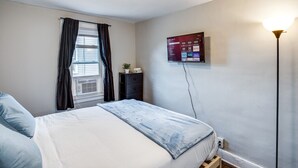 A bedroom with a bed, a dresser, a TV mounted on the wall, and a window with curtains. - Downtown Rochester Home / 3 Bedrooms, Parking (Rochester)