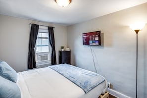 A bedroom with a bed, a dresser, a TV mounted on the wall, and a window with curtains. - Downtown Rochester Home / 3 Bedrooms, Parking (Rochester)