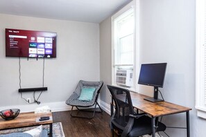 A living room with a flat-screen TV mounted on the wall, a wooden coffee table, a black office chair, and a small table with a remote control. - Downtown Rochester Home / 3 Bedrooms, Parking (Rochester)